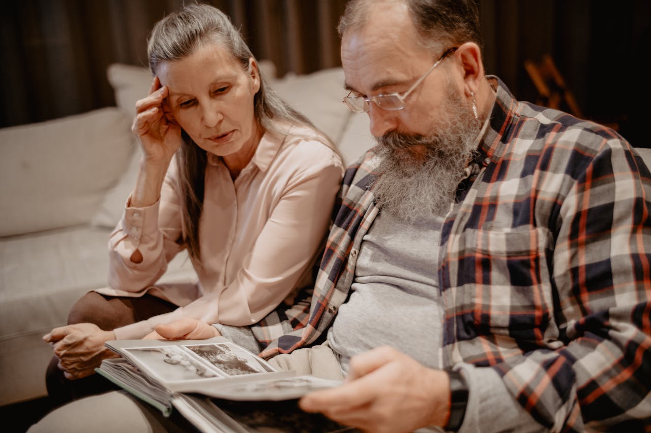 A senior couple reminisces while looking through a photo album at home, reflecting on cherished memories.